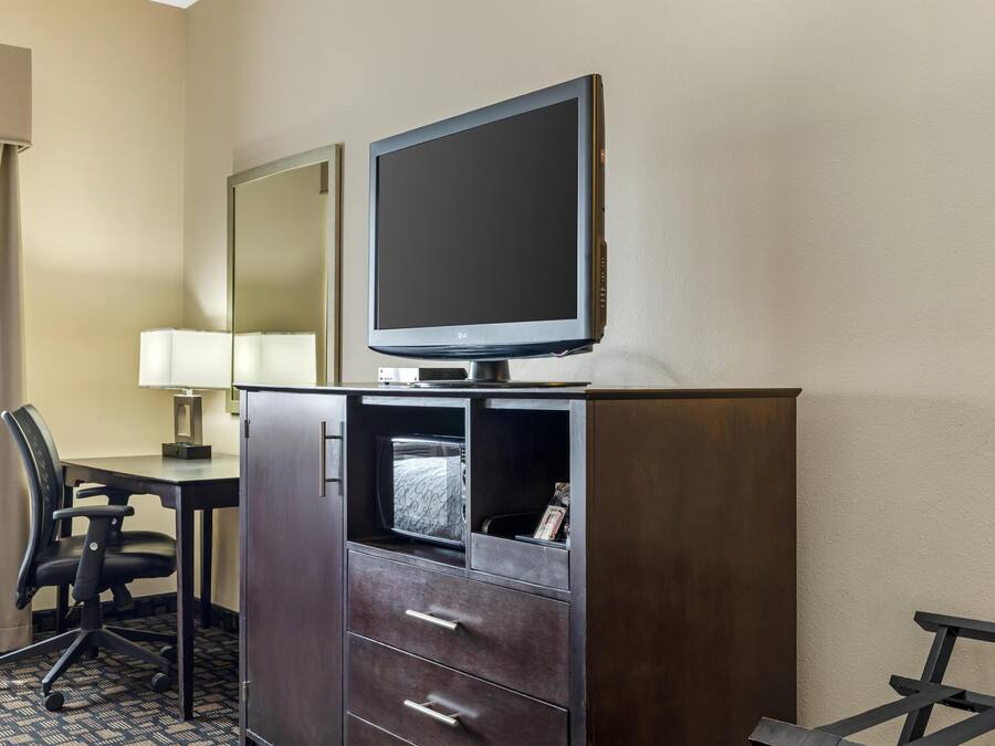 A hotel room with a dark wooden desk, a flat-screen TV, a chair, a lamp, and a mirror.