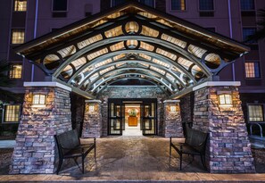 A hotel entrance with a stone facade, arched roof, and two benches.