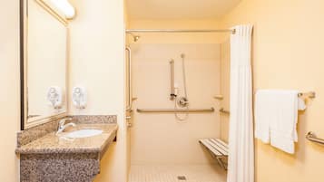 A handicap-accessible bathroom with a granite countertop sink, a mirror, a shower with grab bars, and a white towel hanging on a rack.