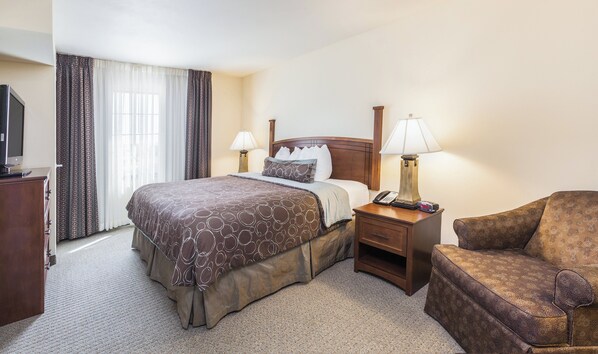 A hotel room with a bed, bedside lamps, a chair, and a television.