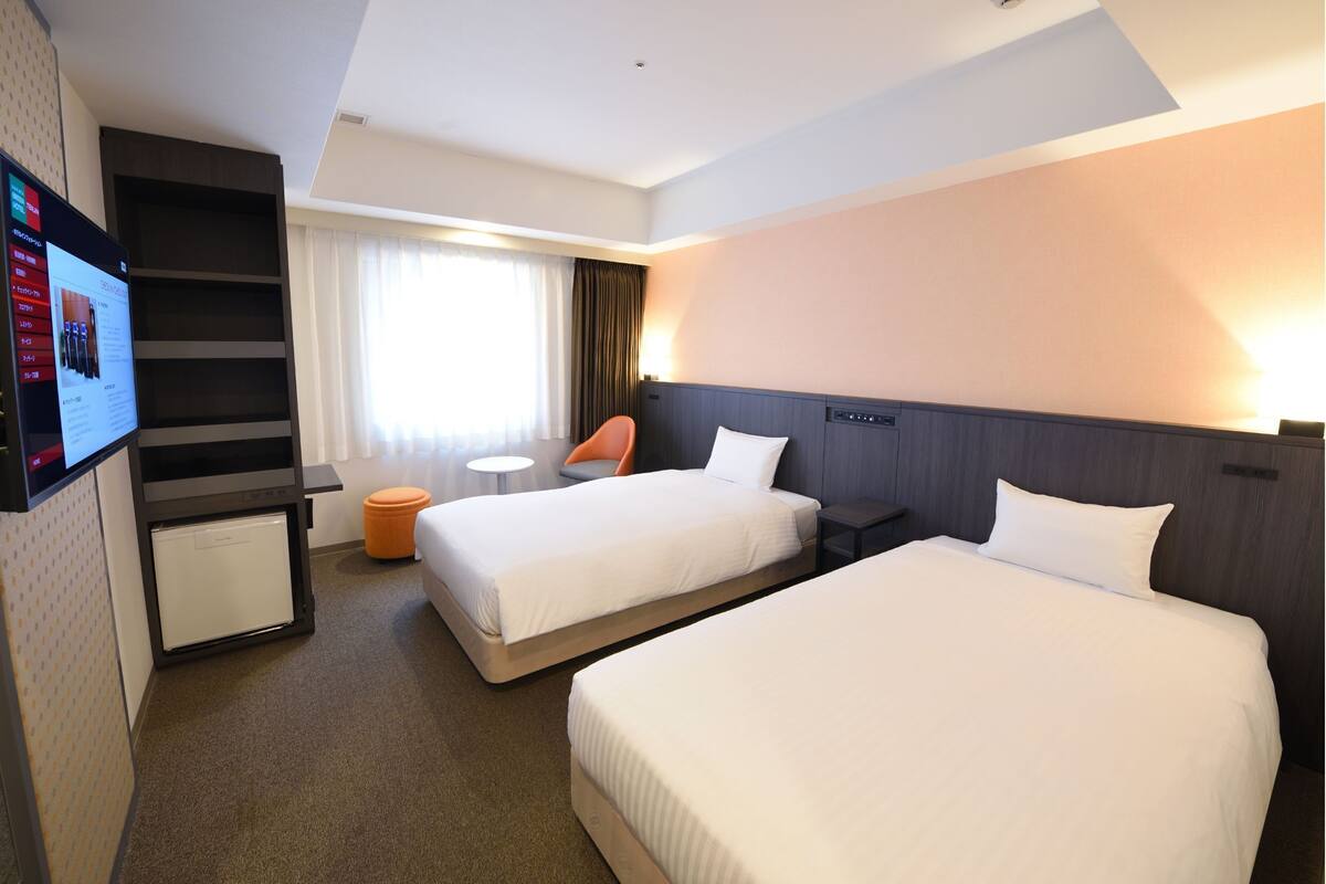 A hotel room with two beds, a desk, a chair, and a TV.