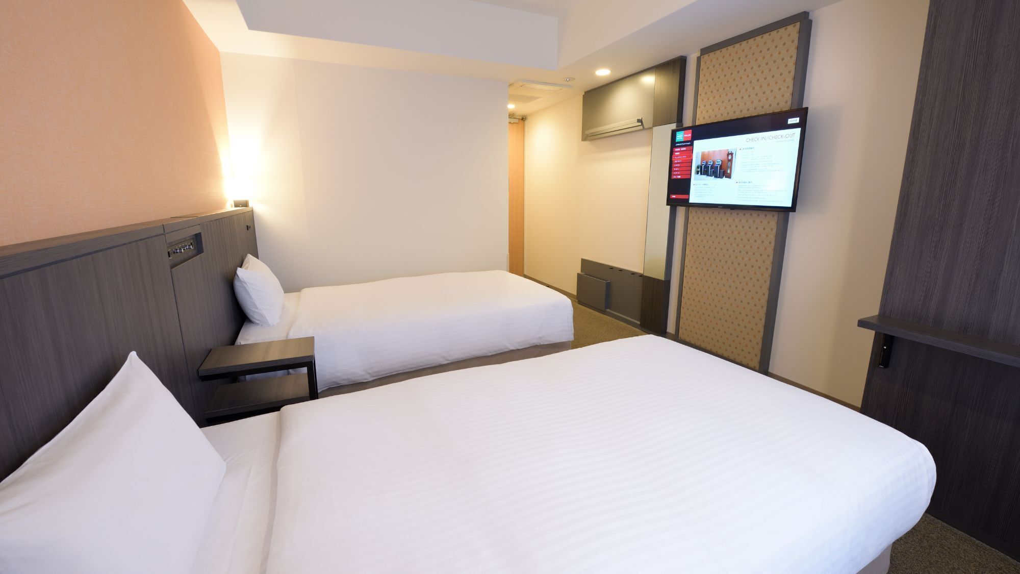 A hotel room with two beds, a TV mounted on the wall, and a desk.