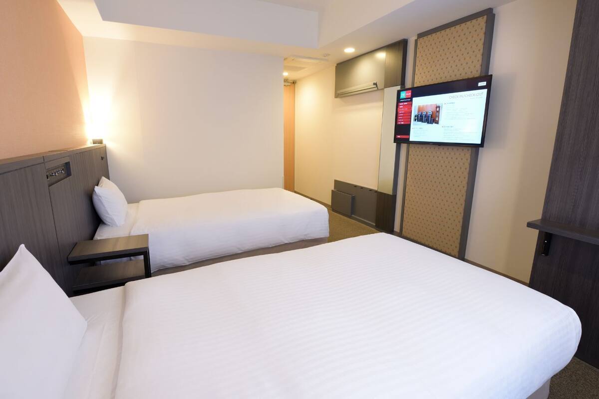 A hotel room with two beds, a TV mounted on the wall, and a desk.