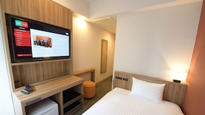Ein Hotelzimmer mit Bett, Schreibtisch mit Computer, Wandfernseher und kleinem Papierkorb.