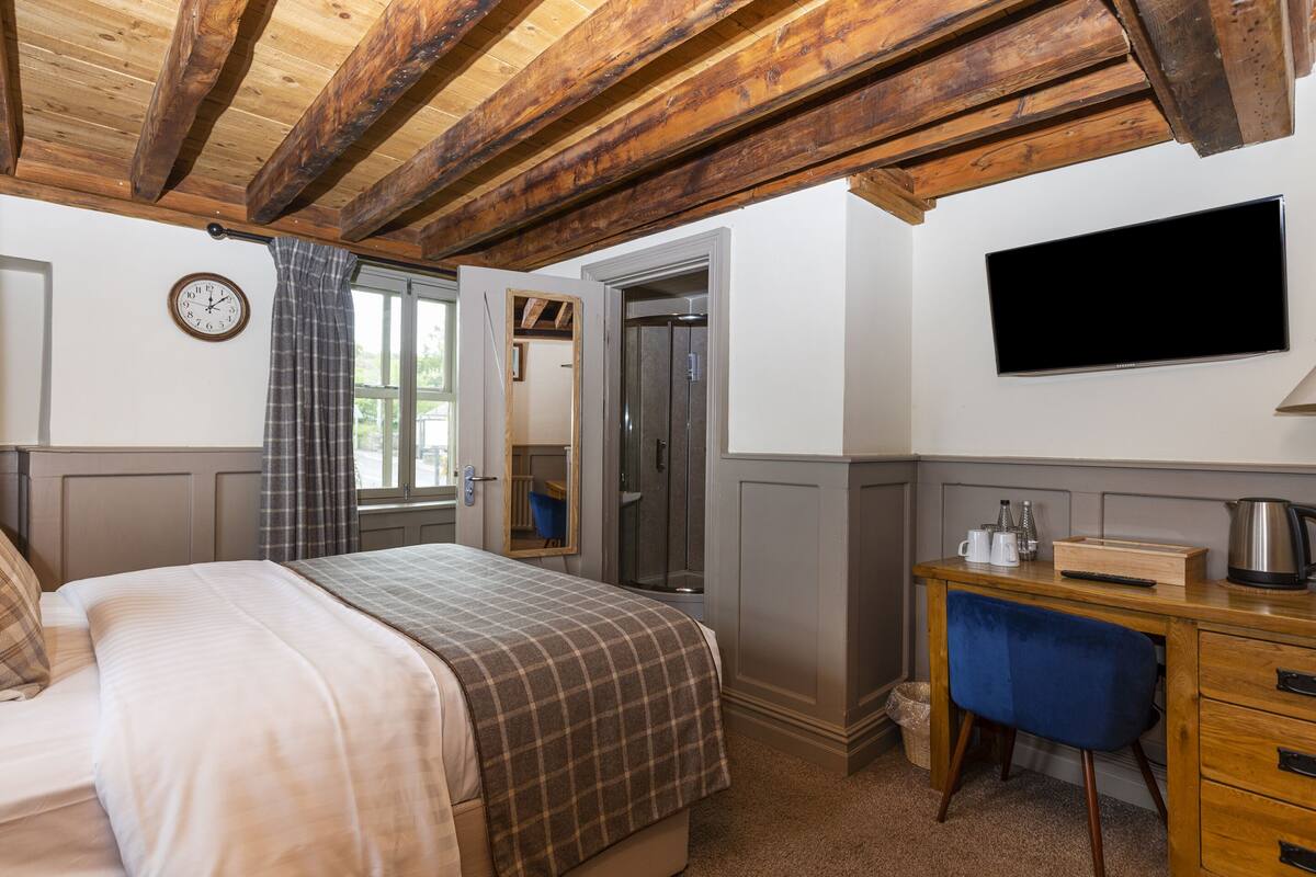 A bedroom with a bed, a desk, a chair, a television, and a clock on the wall.