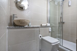 A modern bathroom with a large vessel sink, a toilet, and a glass-enclosed shower area.