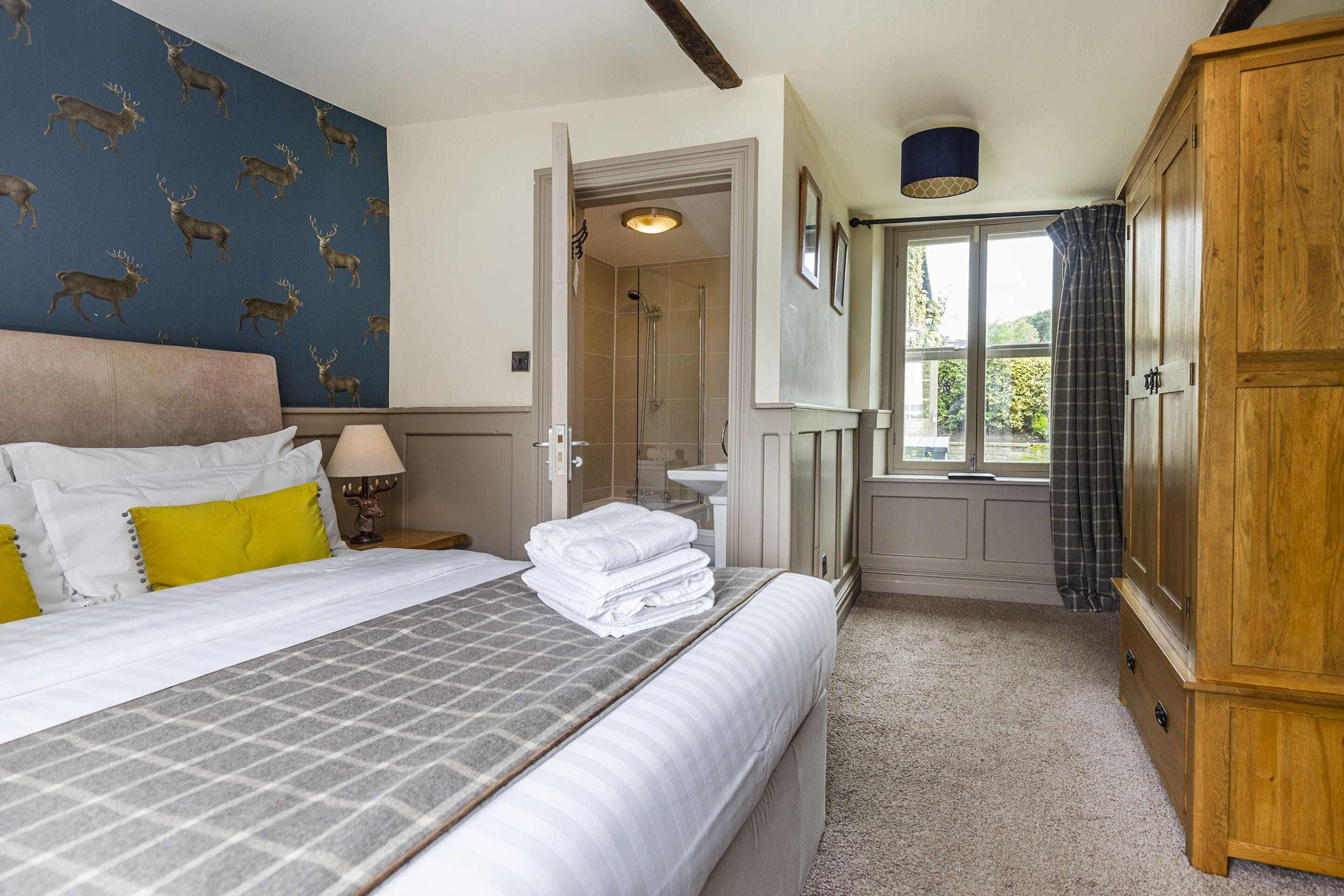 Une chambre à coucher comprenant un lit, une table de chevet, une armoire, une salle de bain avec douche et une fenêtre avec des rideaux.