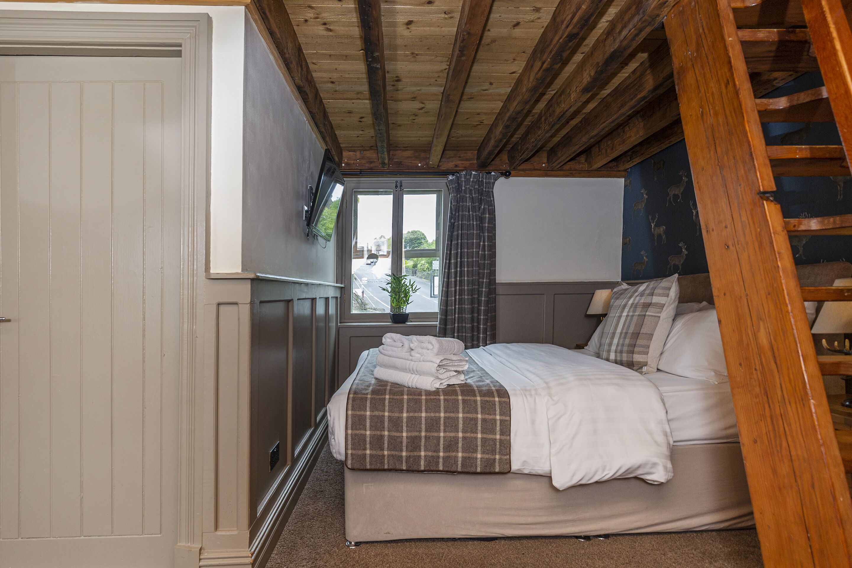 A bedroom with a bed, a window with curtains, a wooden ceiling, and a door.
