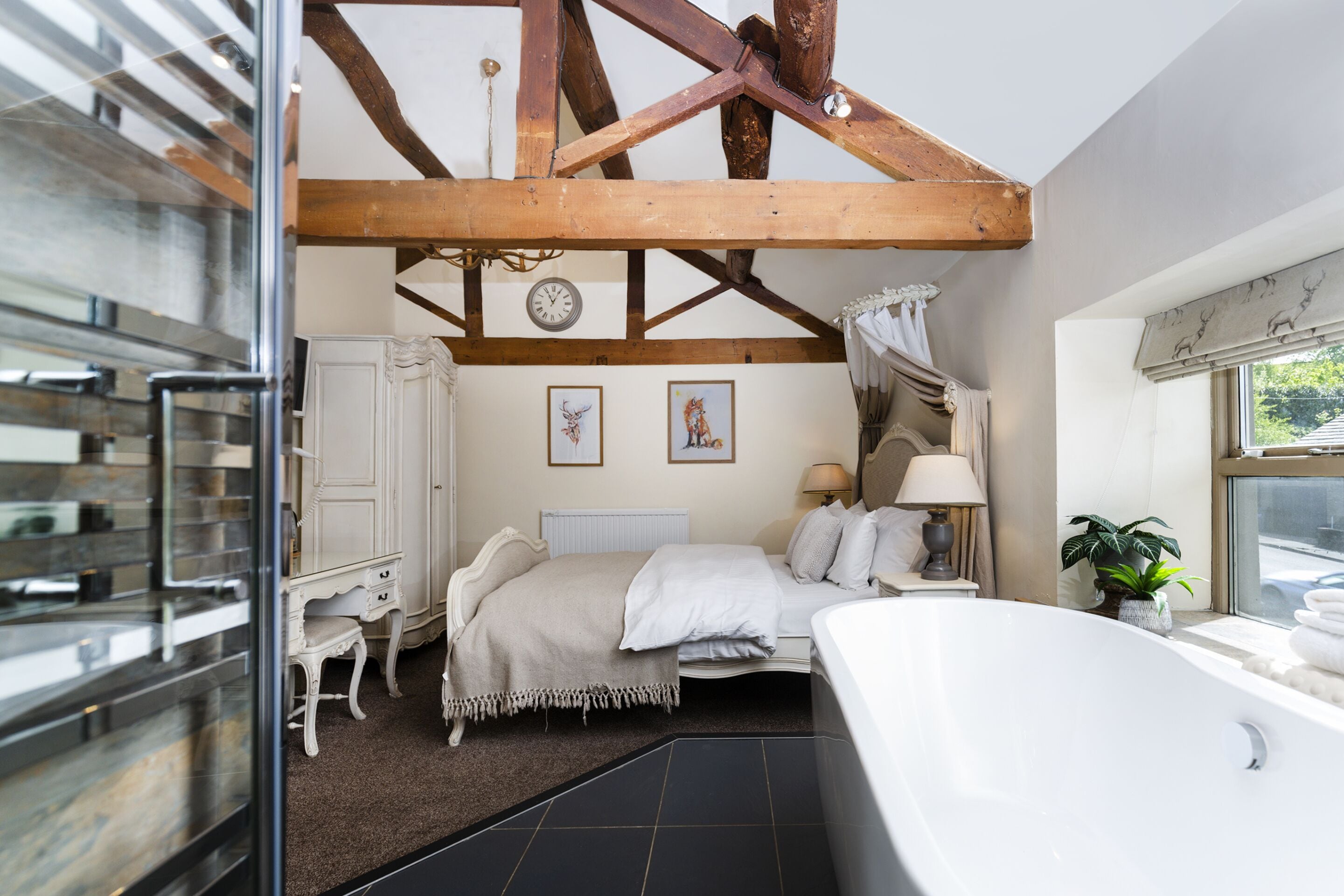A bedroom with a large bed, a white dresser, a vanity, a window with curtains, and a view of the outside.