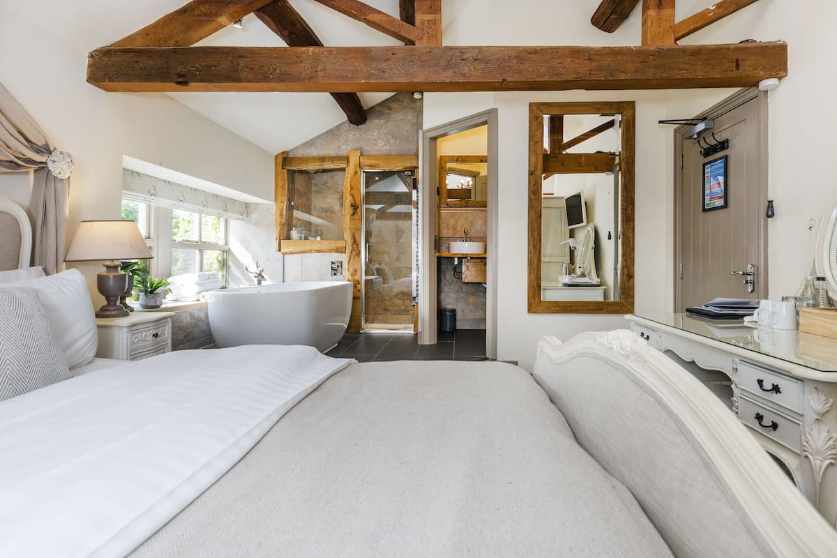 A bedroom with a large bed, a nightstand, a lamp, a dresser, and a bathroom visible through an open door.