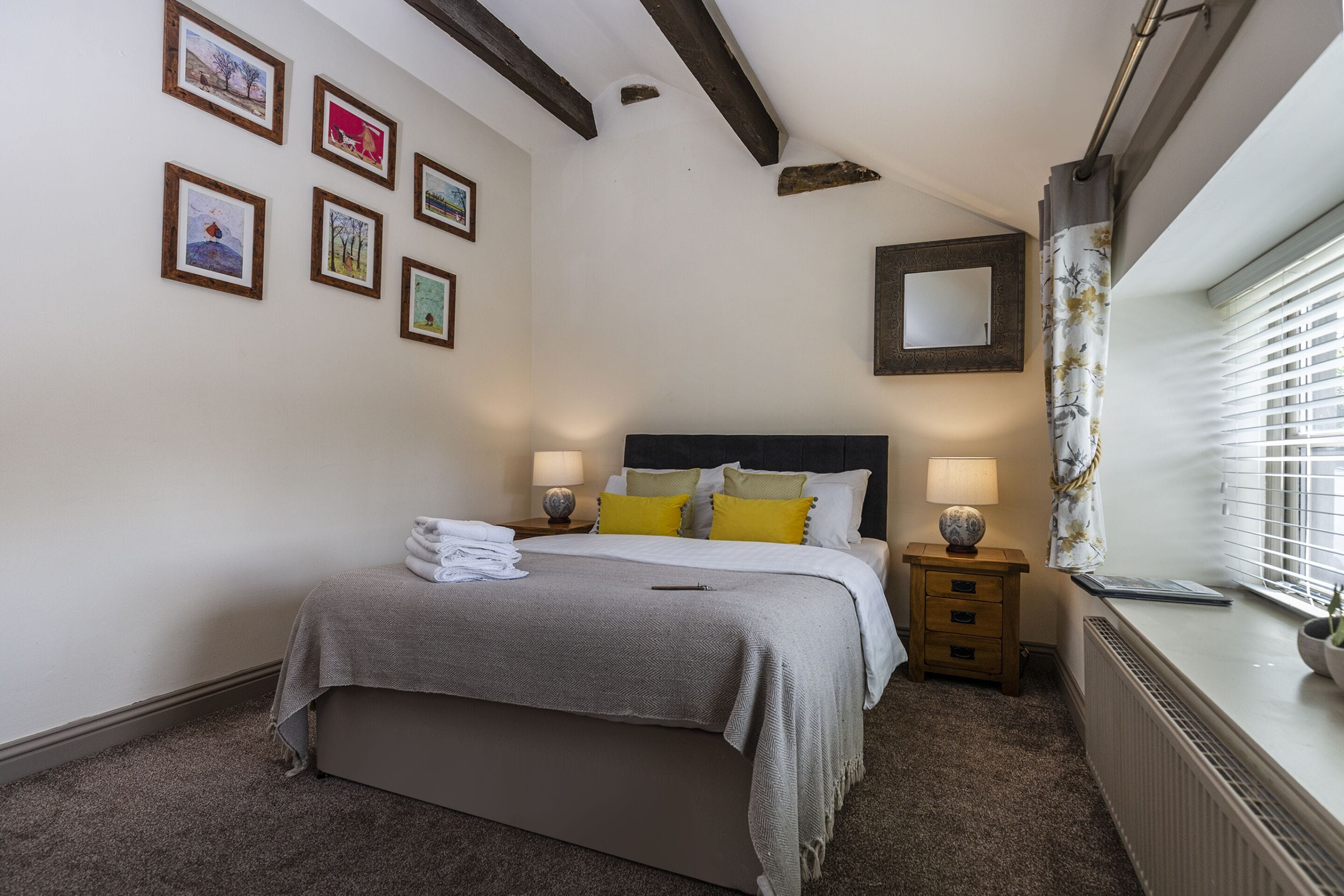 A bedroom with a bed, bedside tables, a nightstand, a mirror, and framed pictures on the wall.