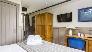 A hotel room with a bed, a wooden wardrobe, a desk with a lamp, a television, and a framed picture on the wall.