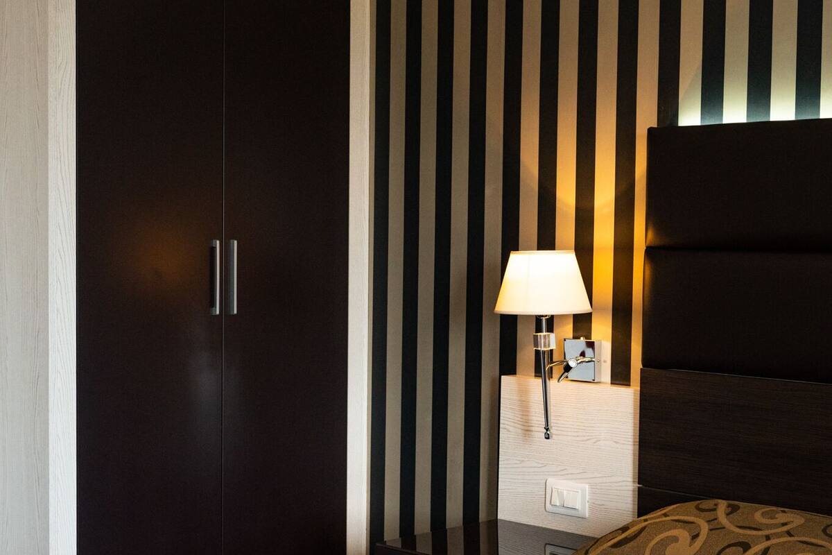 A hotel room with a dark wardrobe, a bedside table with a lamp, and a patterned bedspread.