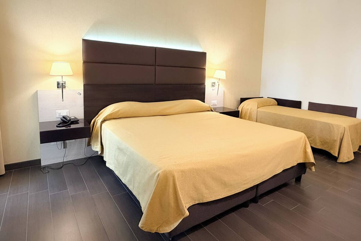A hotel room with two beds, a nightstand with a phone, and wall-mounted lamps.