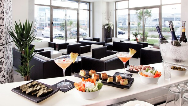 Un moderno vestíbulo de hotel con zonas de estar, un bufé con diversas opciones de comida y un bar con bebidas.