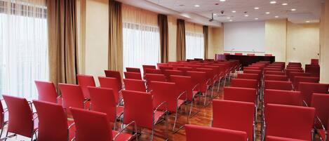Une salle de conférence avec des rangées de chaises rouges, un pupitre et un écran de projection.