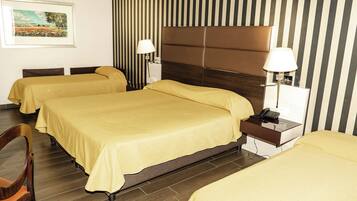 Quarto de hotel com três camas, cada uma com colcha amarela, cabeceira de madeira e mesa de cabeceira com luminária e telefone.