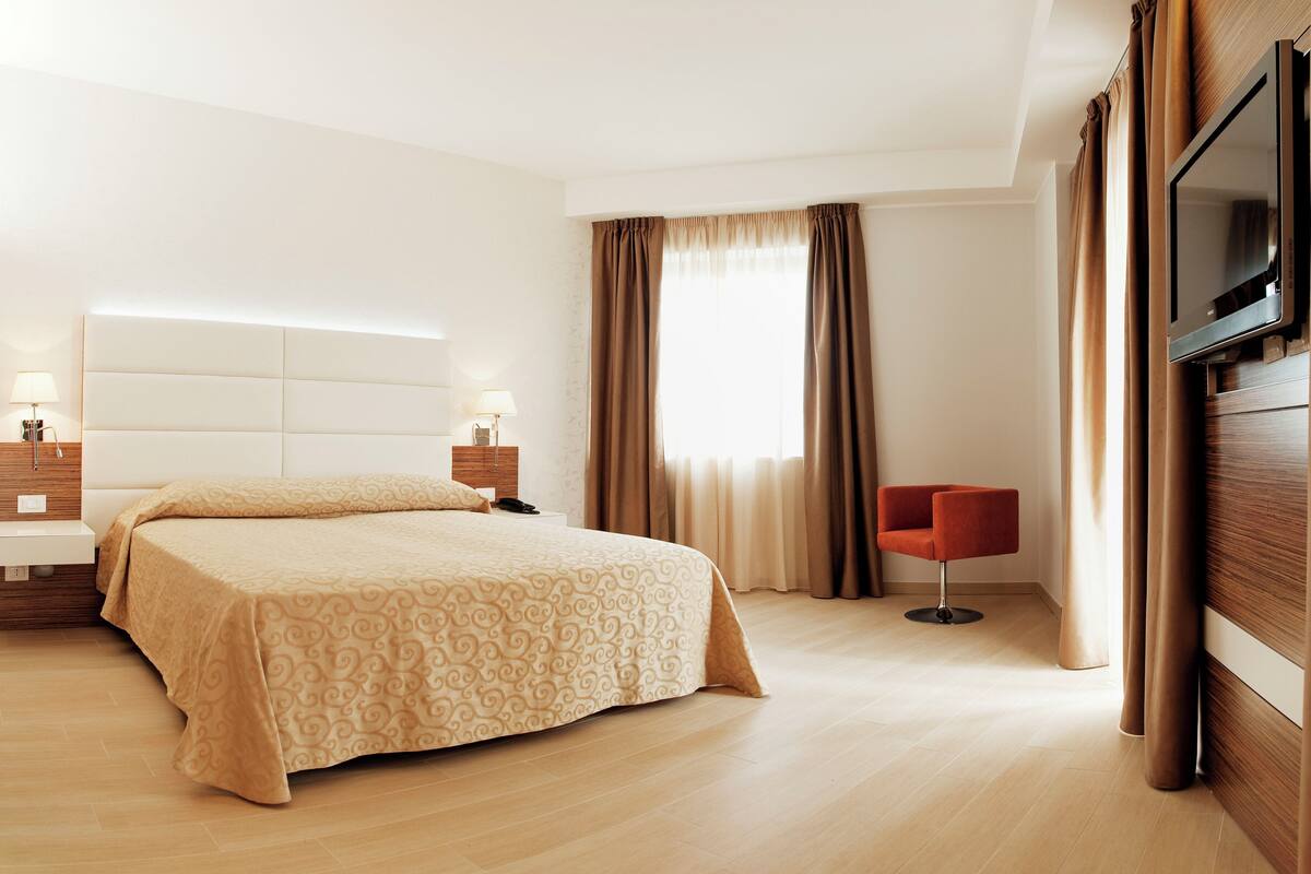 A hotel room with a large bed, a bedside table with a lamp, a TV mounted on the wall, and a chair.
