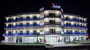 Un hotel de varios pisos con un llamativo letrero 'S Hotel', múltiples balcones y una entrada bien iluminada.