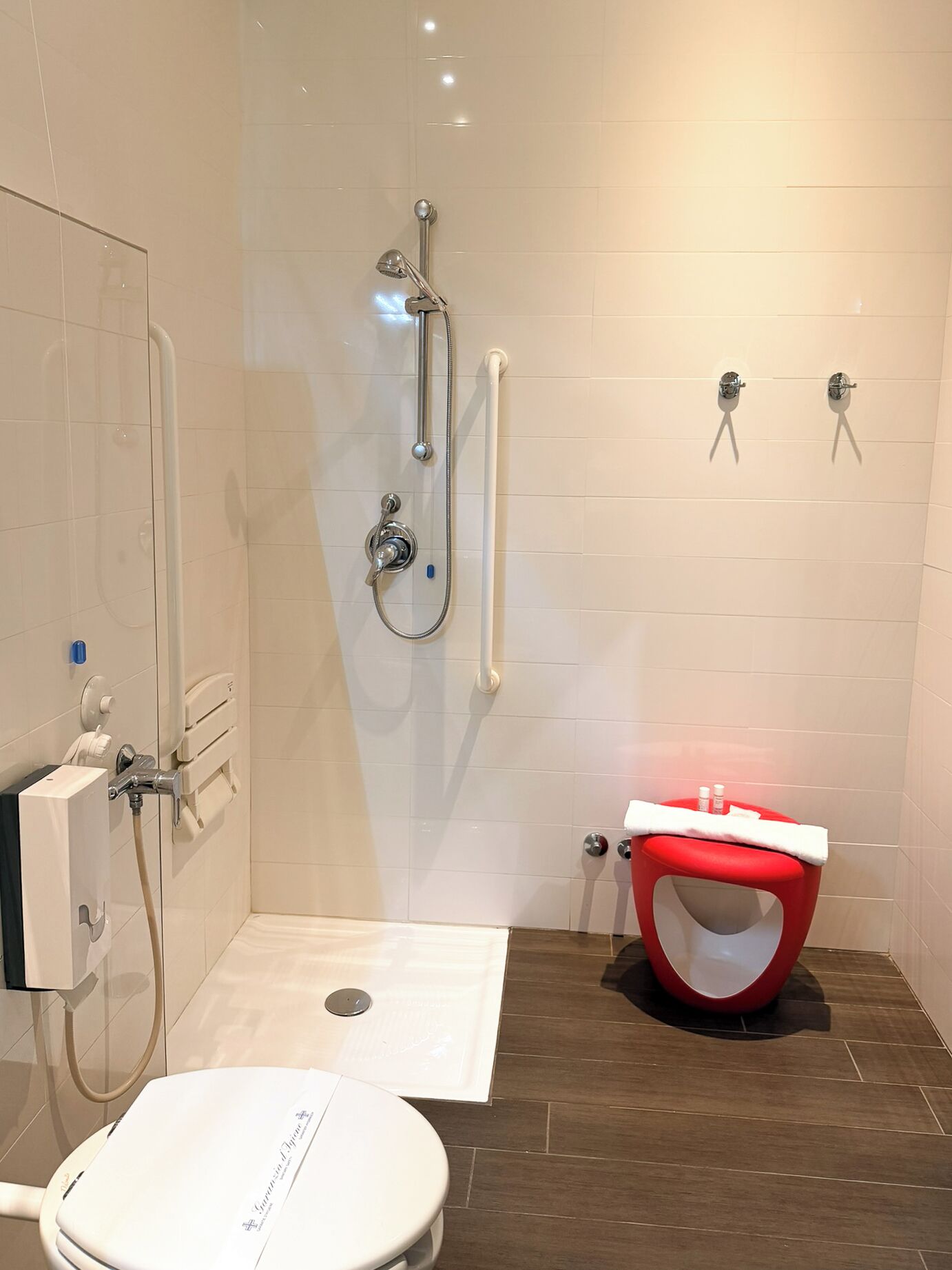 A modern bathroom with a shower, toilet, and a red stool.