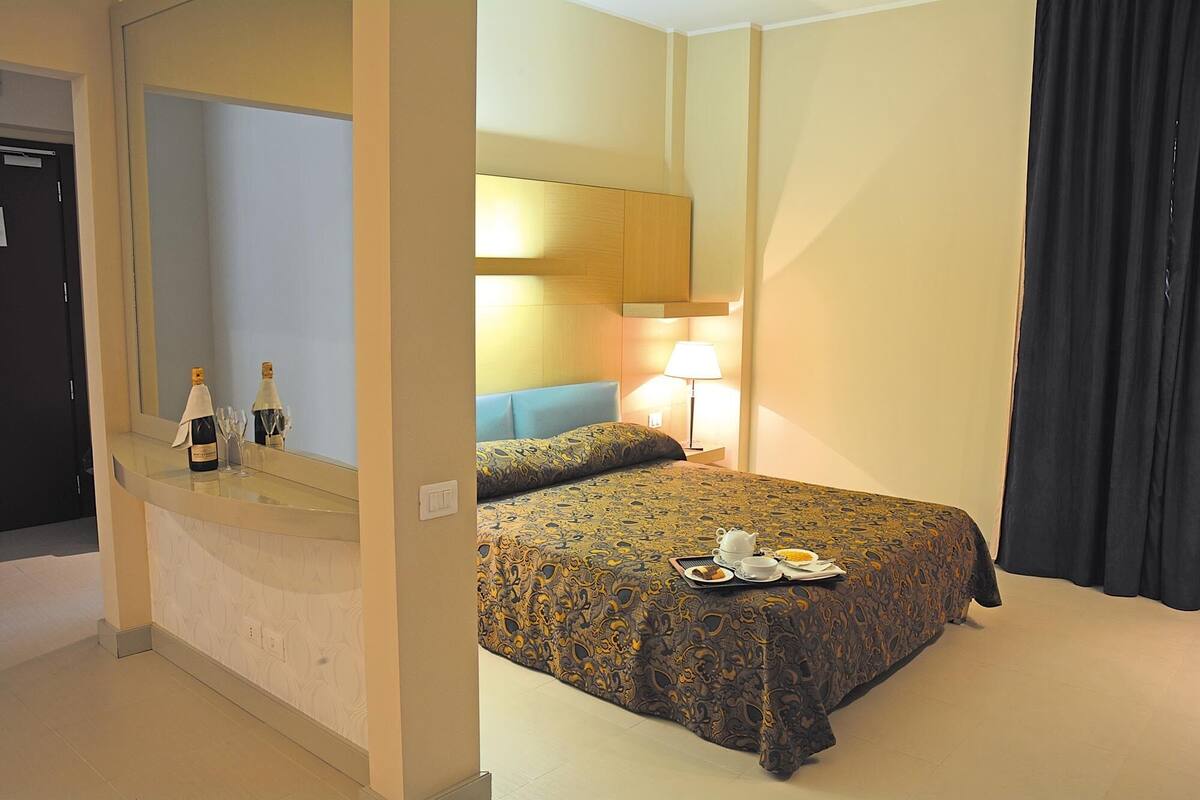 A hotel room with a bed, bedside table, lamp, and a mirror.