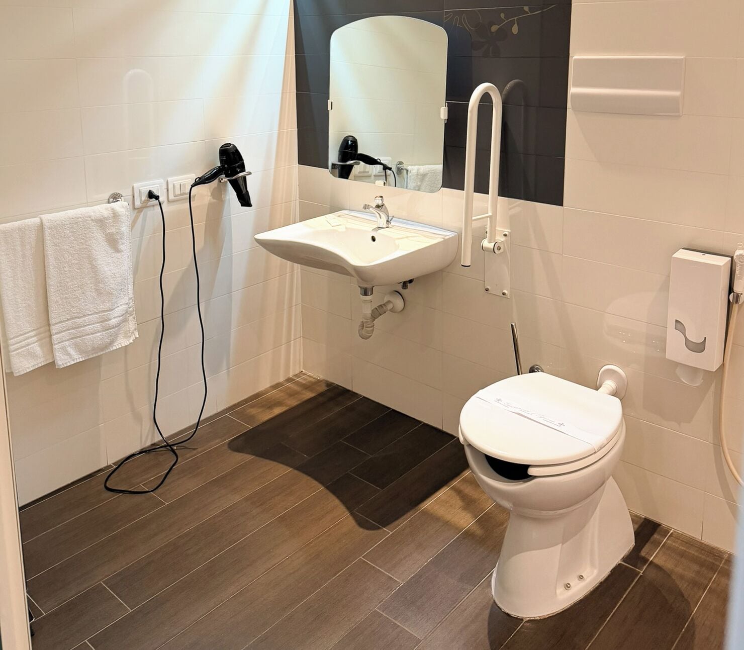 A bathroom with a white sink, a toilet, and a hairdryer on a wall.