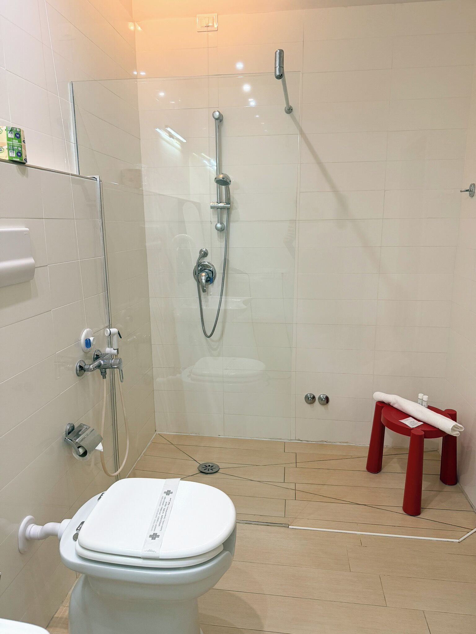 A modern bathroom with a glass shower enclosure, a toilet, and a red stool.