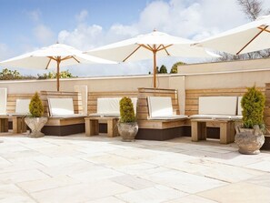 A series of outdoor seating areas with white umbrellas, stone planters, and a tiled floor.