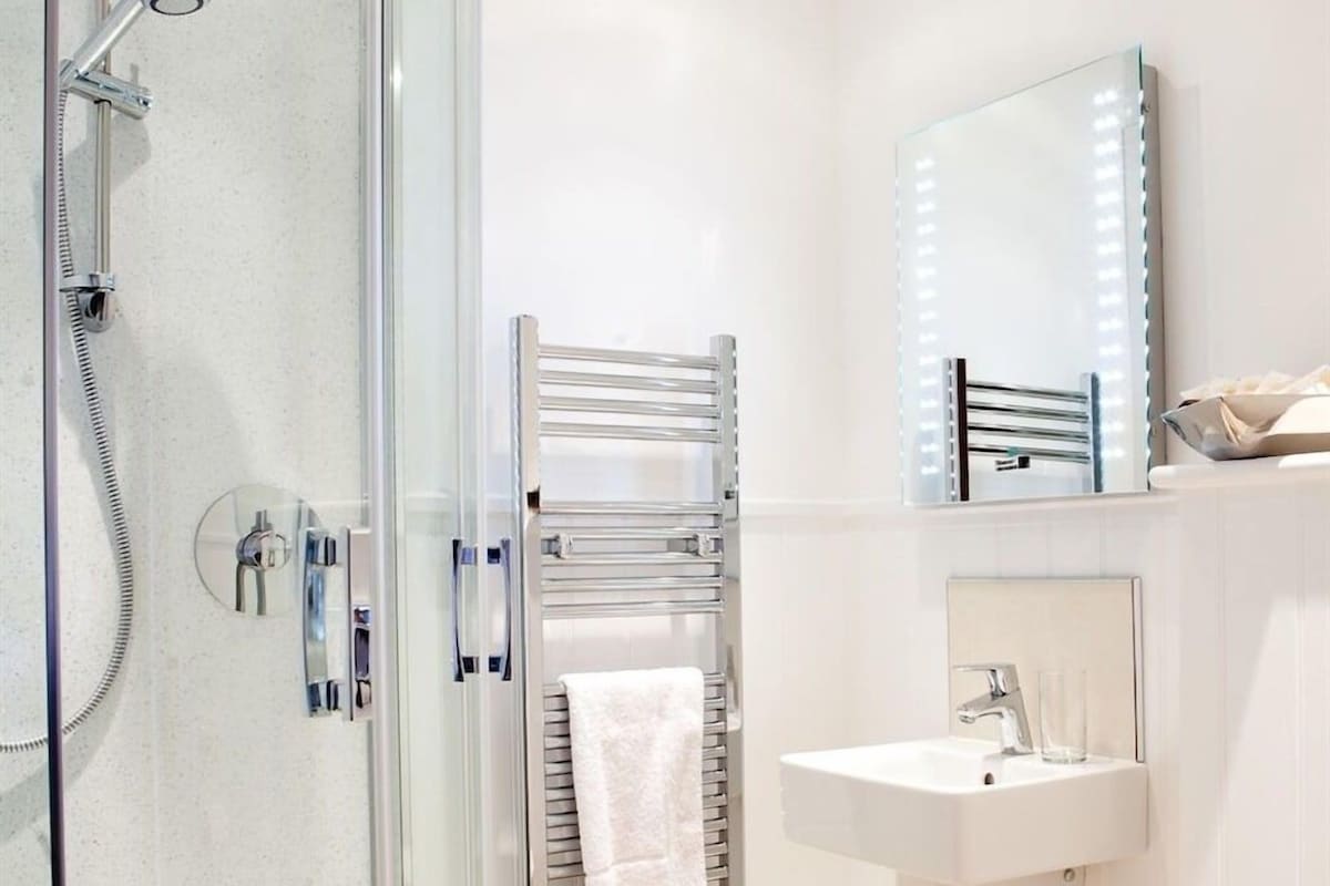 A bathroom with a glass shower enclosure, a towel rack, a mirror with lights, and a sink.