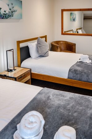 A hotel room with a wooden bed, a bedside table with a lamp, a chair, and a large mirror on the wall.
