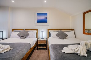 A hotel room with two single beds, a nightstand with a lamp, a framed picture on the wall, and a mirror on the right wall. - The Victoria Inn (Truro)