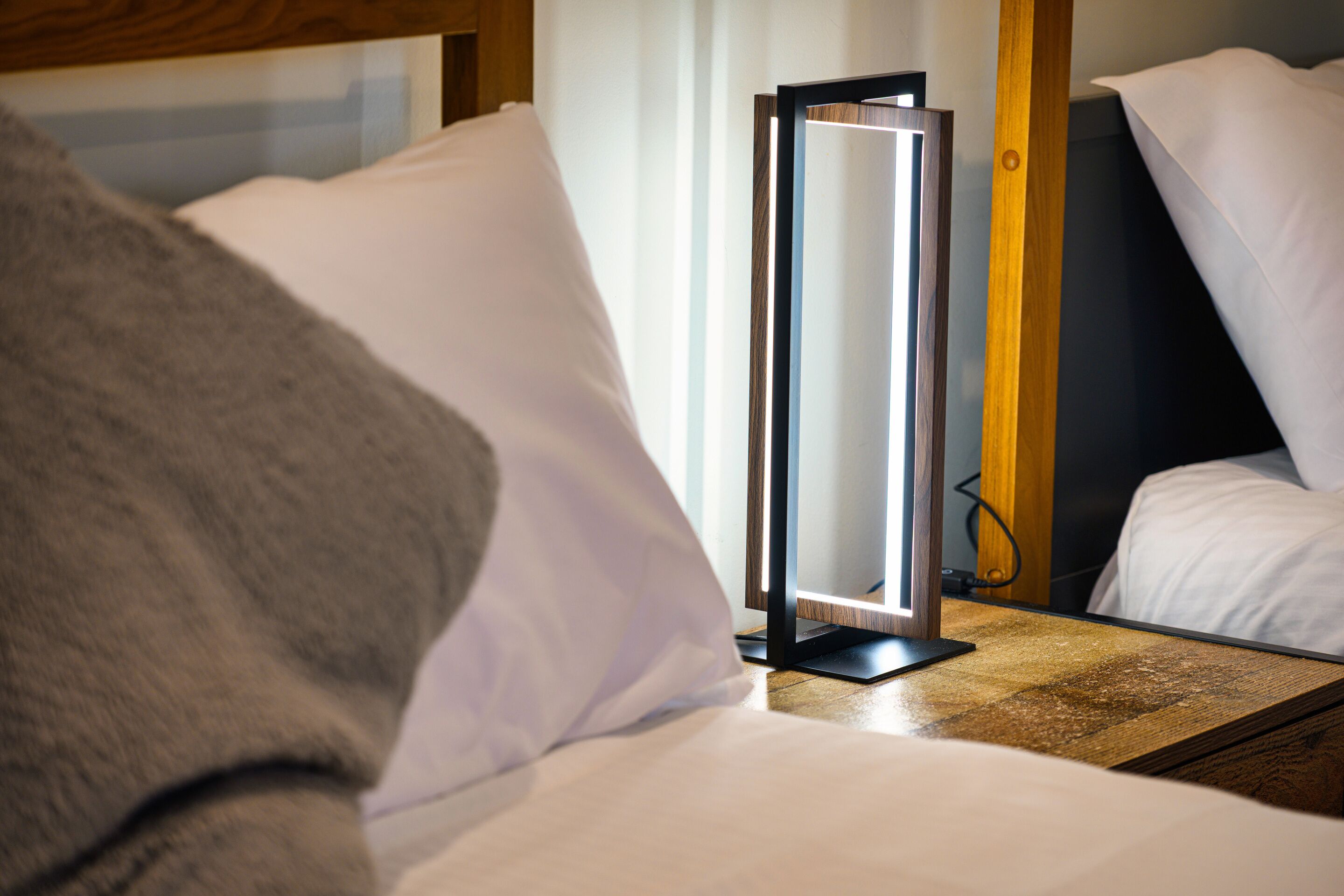 A hotel room with a bed, a bedside table, a bedside lamp, and a window with curtains.