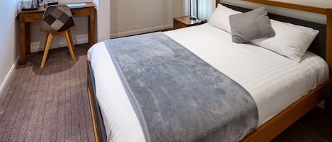 A hotel room with a bed, a desk, a chair, a nightstand, and a window.