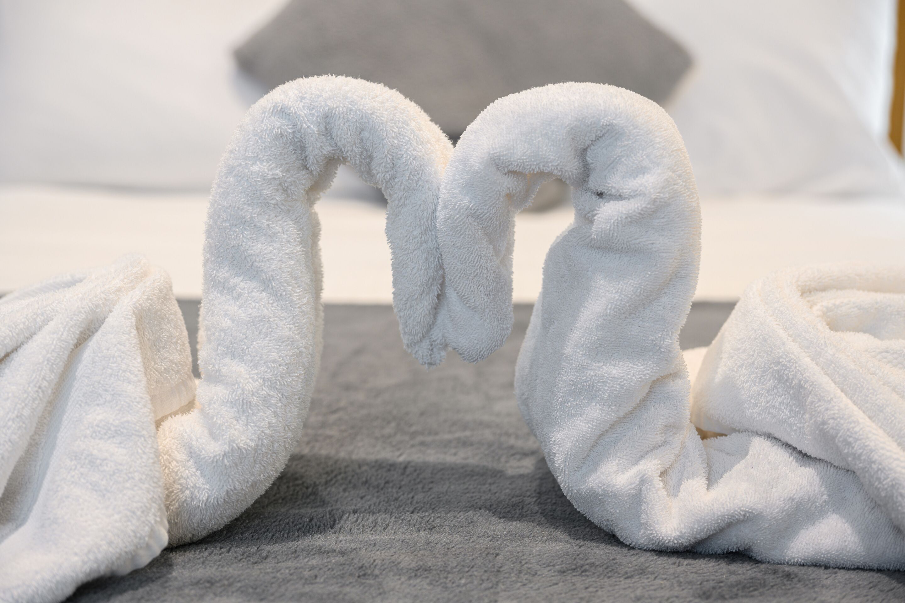 Two white towels arranged in a heart shape on a gray carpet.