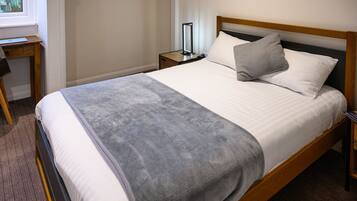 Una cama bien tendida con una manta gris, un cabecero de madera y una mesita de noche con una lámpara.