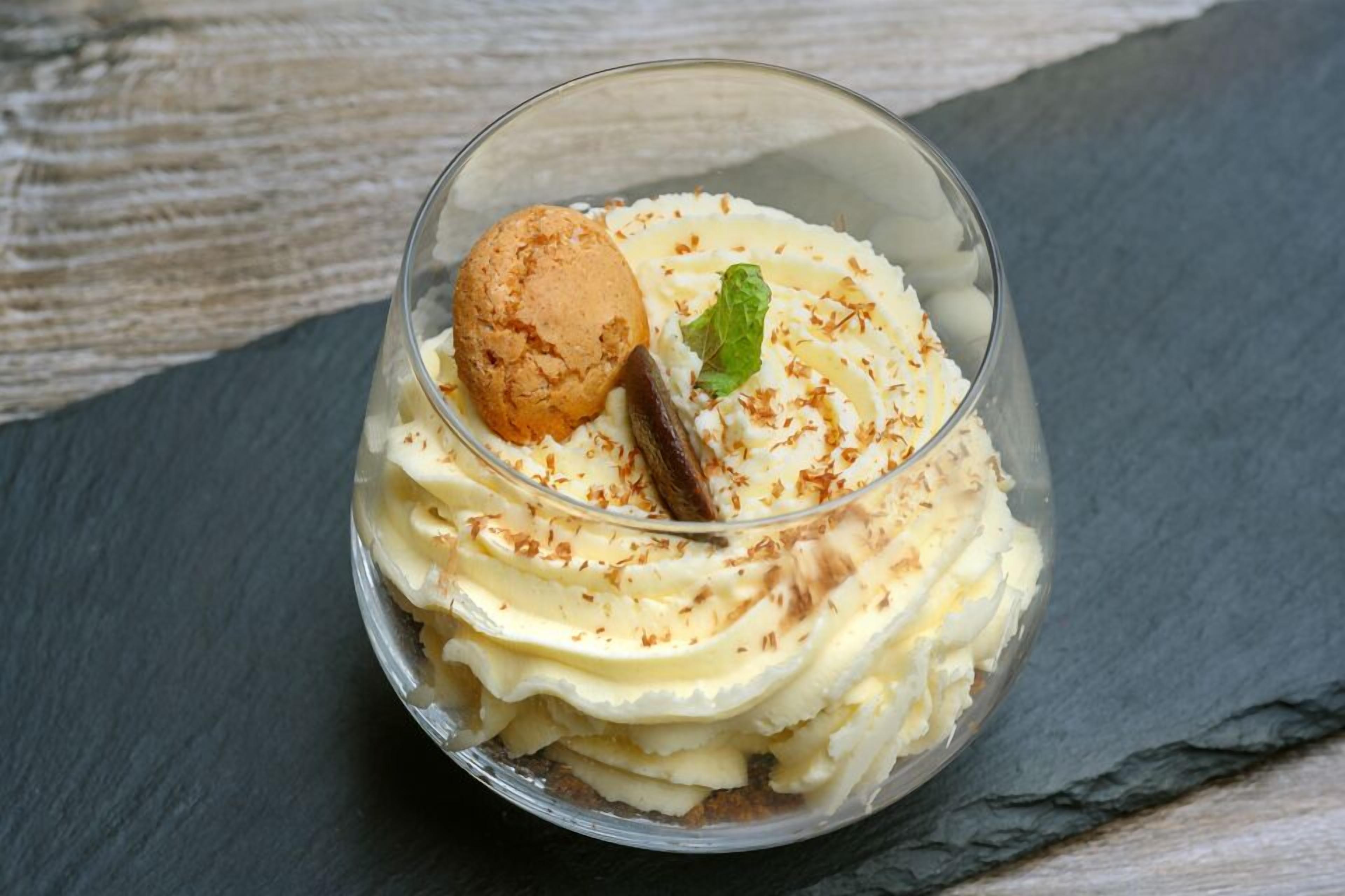 A dessert in a clear glass with whipped cream and a cookie on top, placed on a slate surface.
