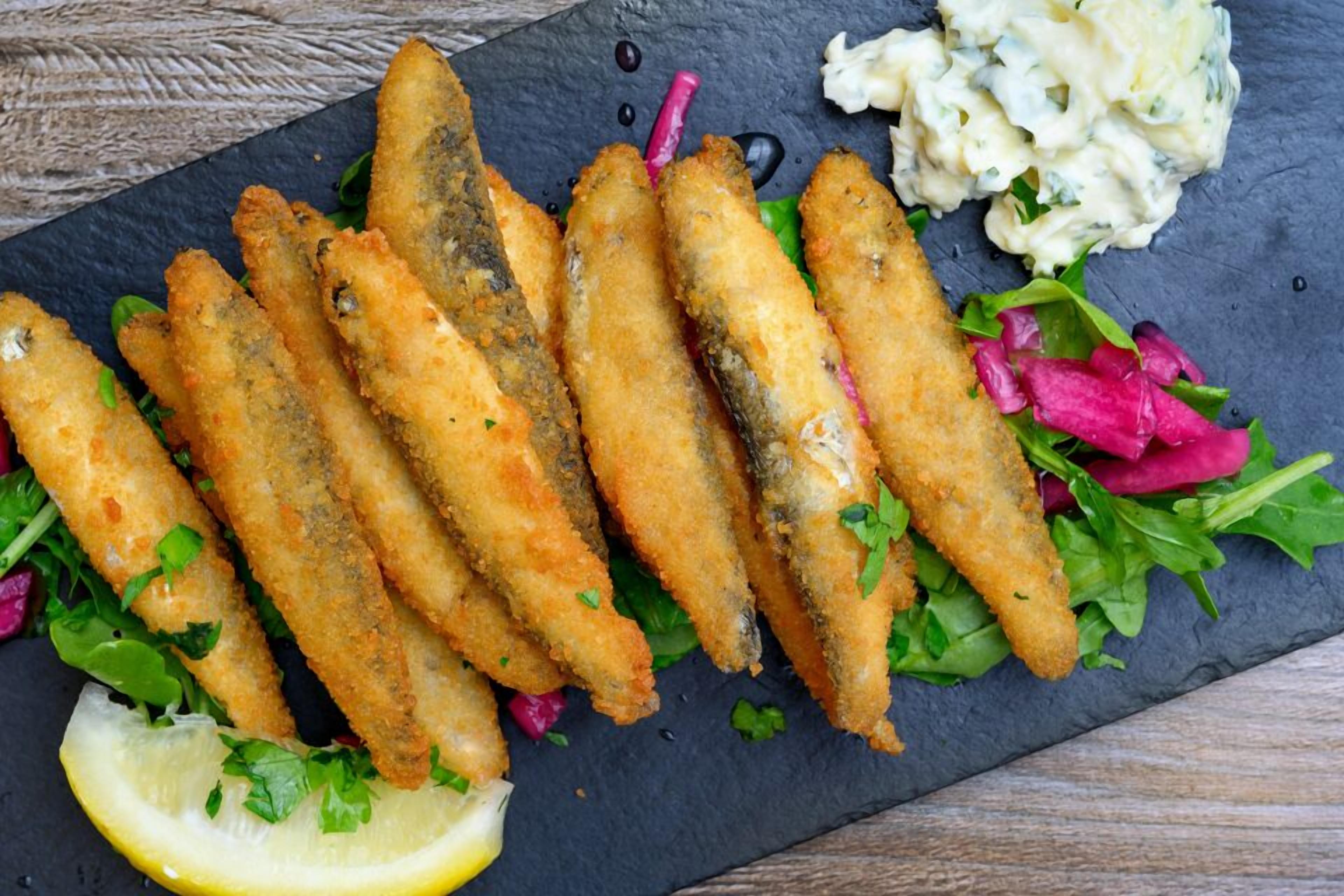 A plate of breaded fish sticks with a side of creamy sauce and a salad.