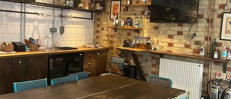 A kitchen with a wooden table and blue chairs, a brick wall, and a mounted TV.