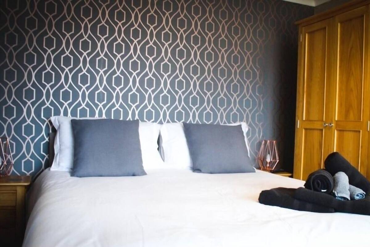 A neatly made bed with two pillows, a wooden wardrobe, and a folded towel on the side.