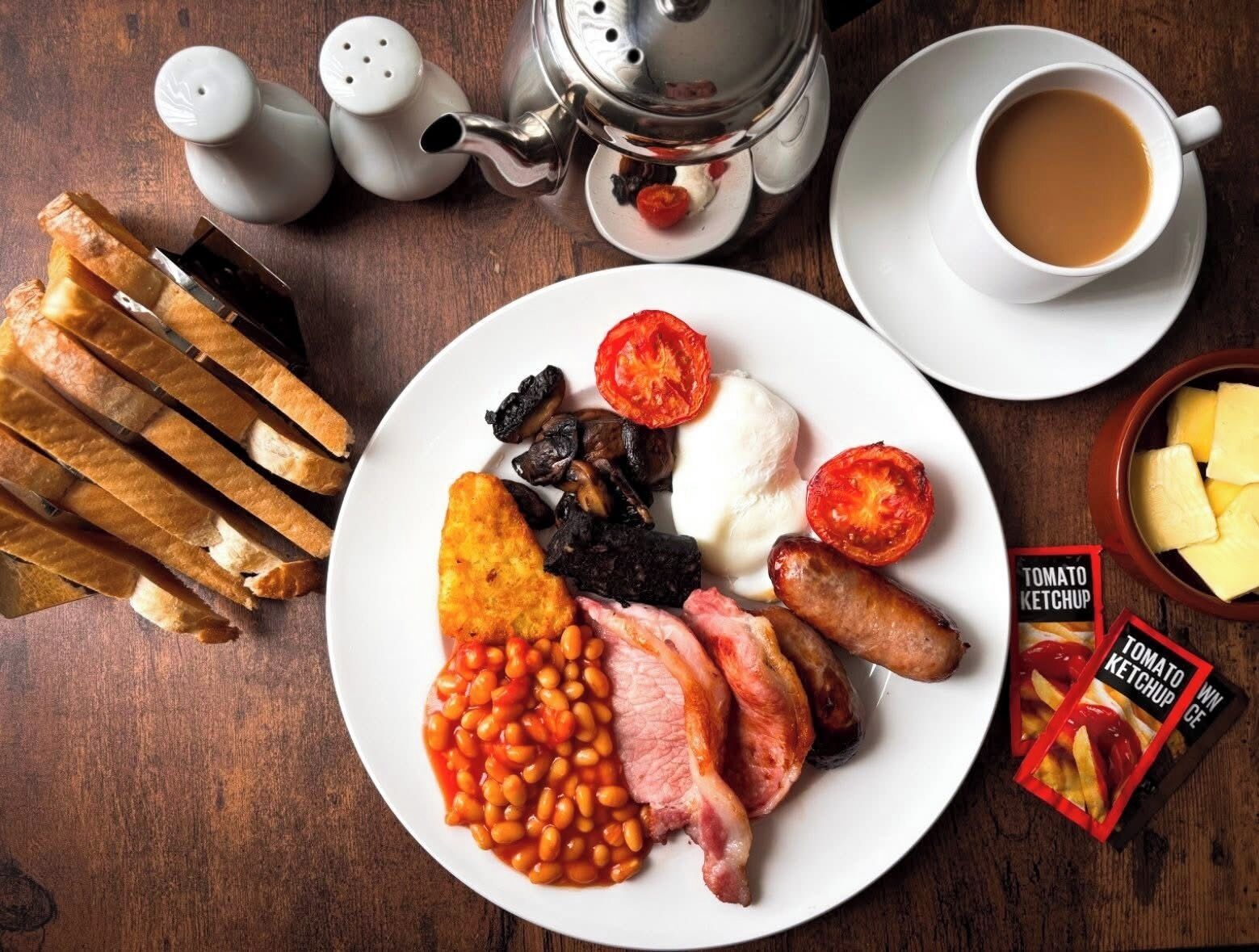A plate of breakfast food, a teapot, salt and pepper shakers, a cup of coffee, and a box of tomato ketchup.