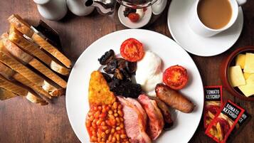 A plate of breakfast food, a teapot, salt and pepper shakers, a cup of coffee, and a box of tomato ketchup.