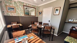 Zona pranzo con tavoli e sedie di legno, uno specchio appeso al muro e quadri incorniciati.