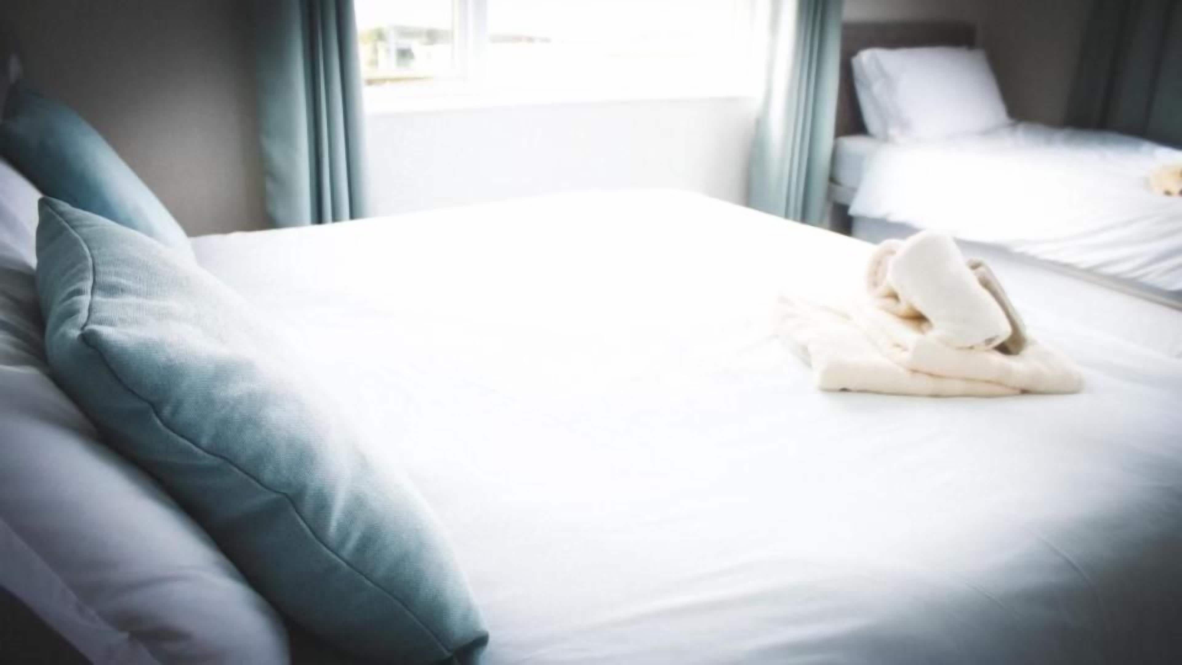 Habitación de hotel con una cama bien tendida, una ventana con cortinas y vista a otra habitación.