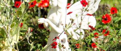 A garden with a white fairy statue surrounded by red flowers and green foliage.