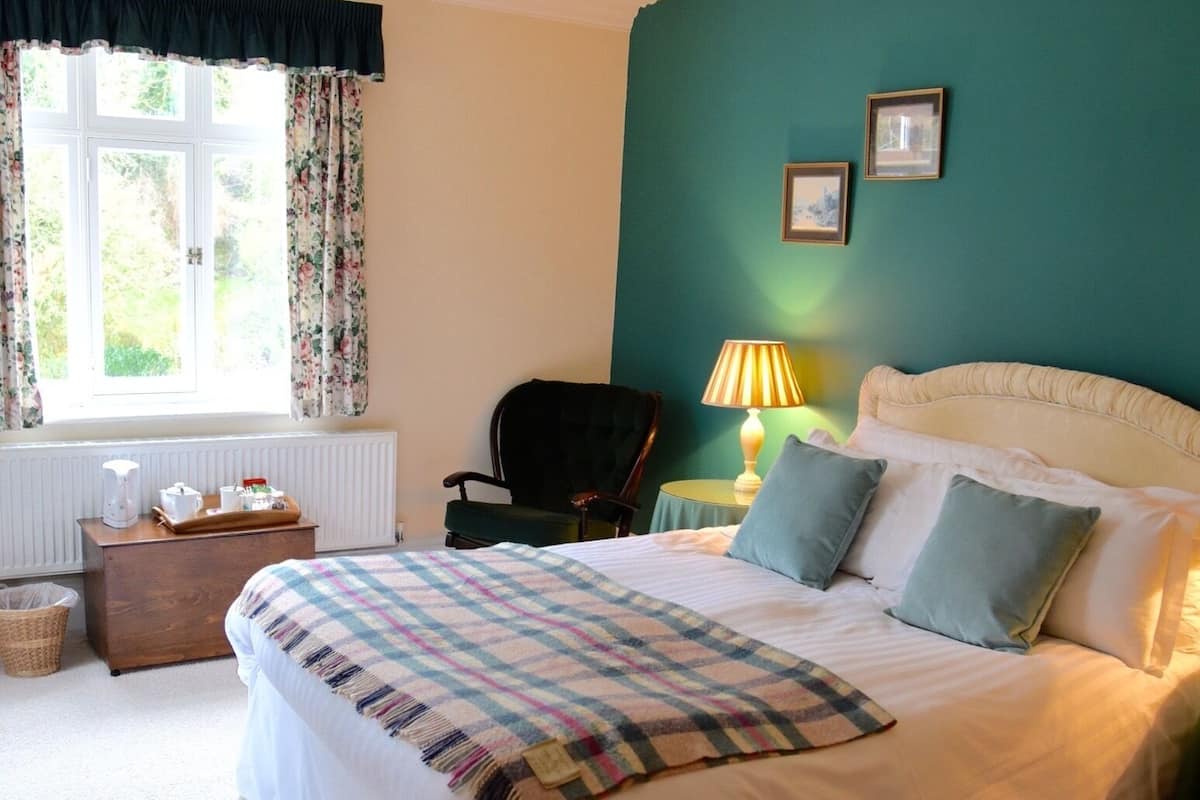 A bedroom with a large bed, a chair, a lamp, and a window with curtains.