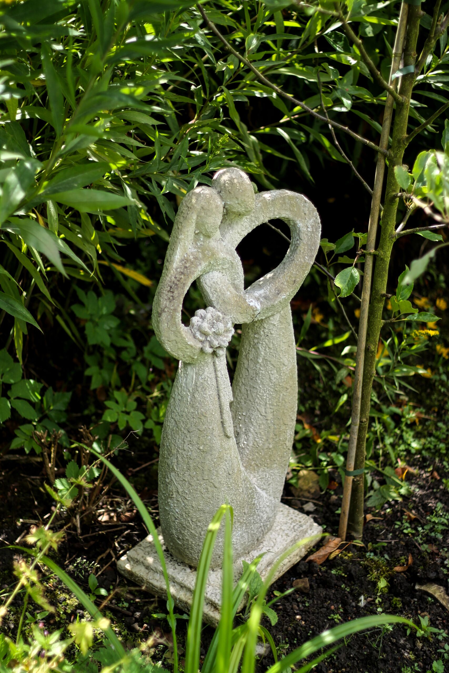 A garden statue of a couple embracing, surrounded by lush greenery.