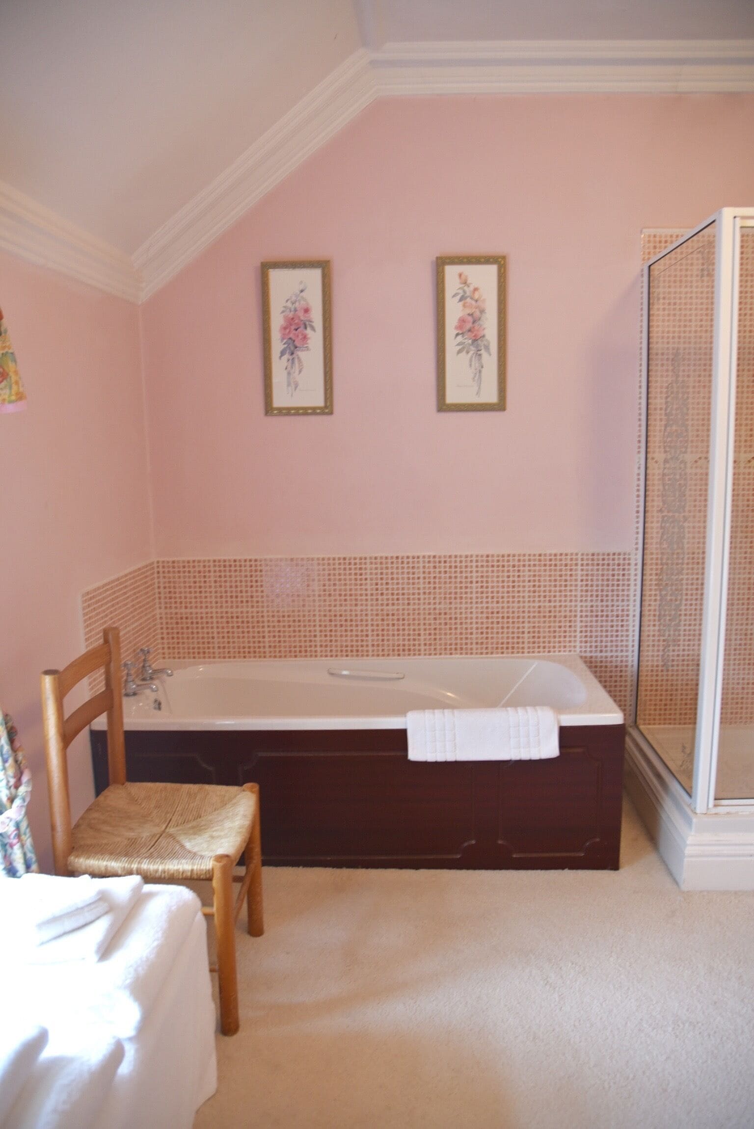 A bathroom with a bathtub, a chair, and two framed floral pictures on the wall.