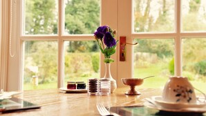 Et bord med en vase fyldt med lilla blomster, salt- og peberkværn, en lille skål og en tekedel.