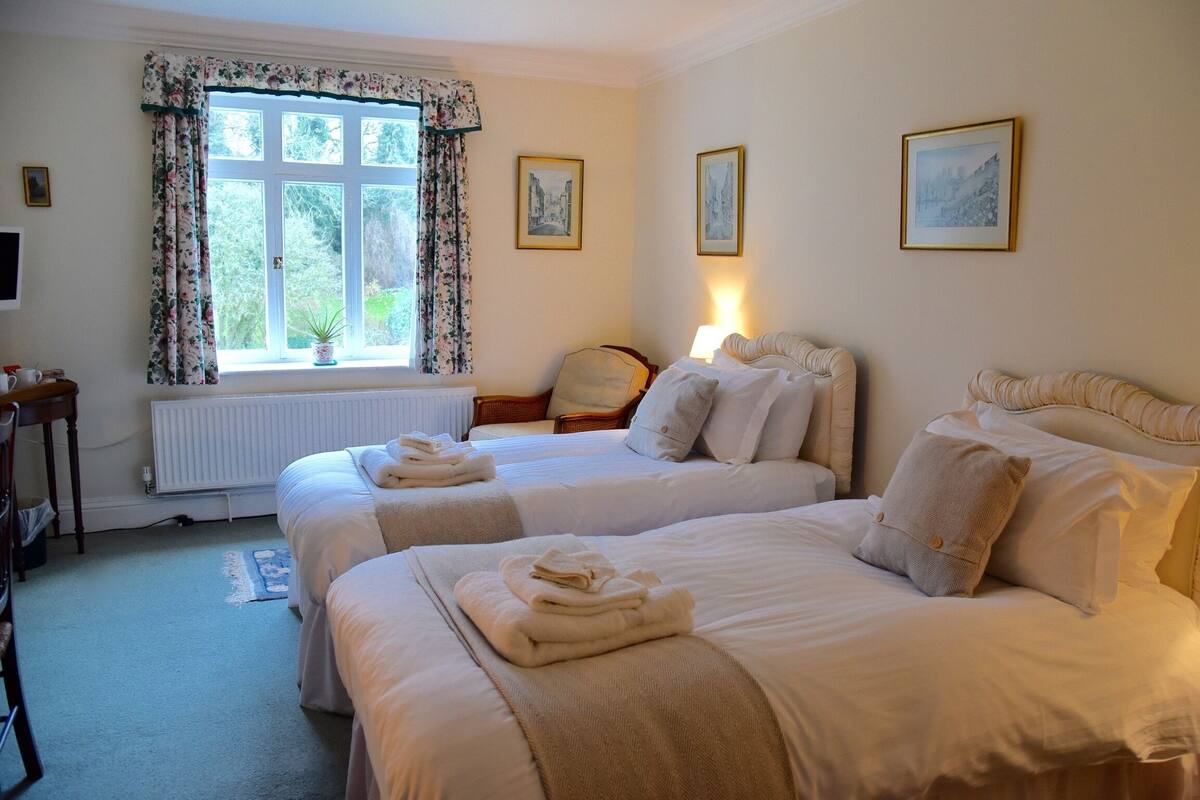 A hotel room with two beds, a radiator, a chair, and a window with curtains.