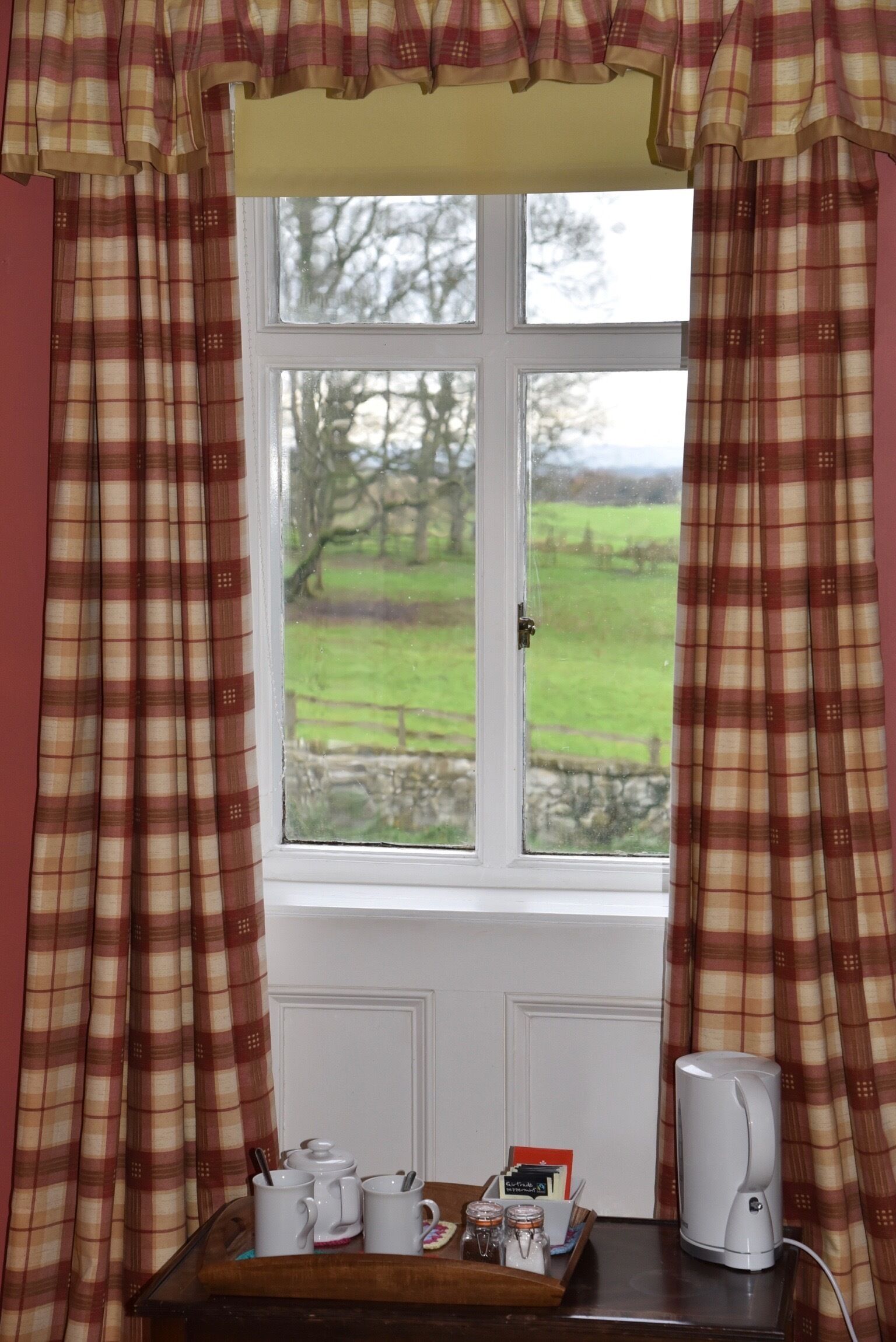 A window with plaid curtains, a white door, and a table with mugs and a kettle.